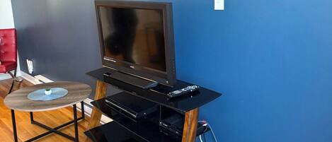 A living room with a TV on a black entertainment unit, a small round table with a plant, and a red chair.