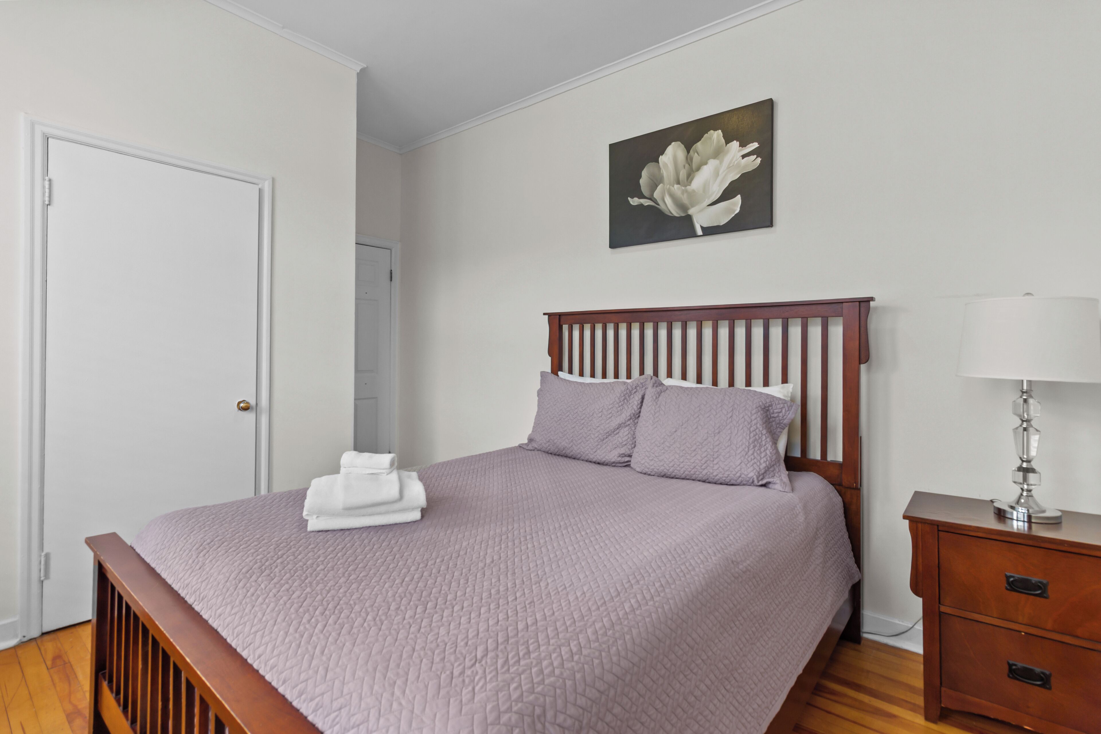 A neatly made bed with a wooden headboard, a bedside table with a lamp, and a painting on the wall.