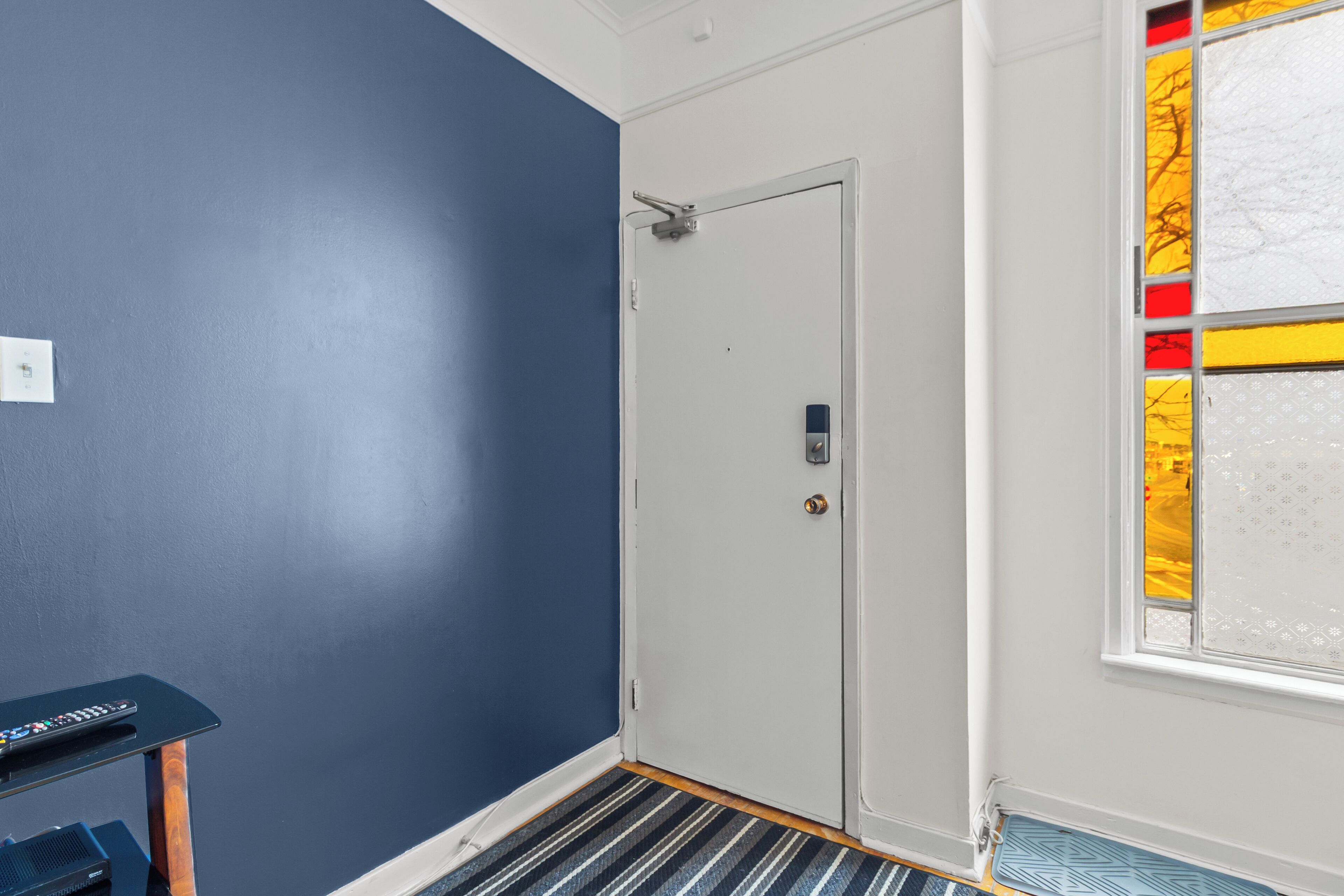 A hallway with a blue wall, a white door, and a window with stained glass.
