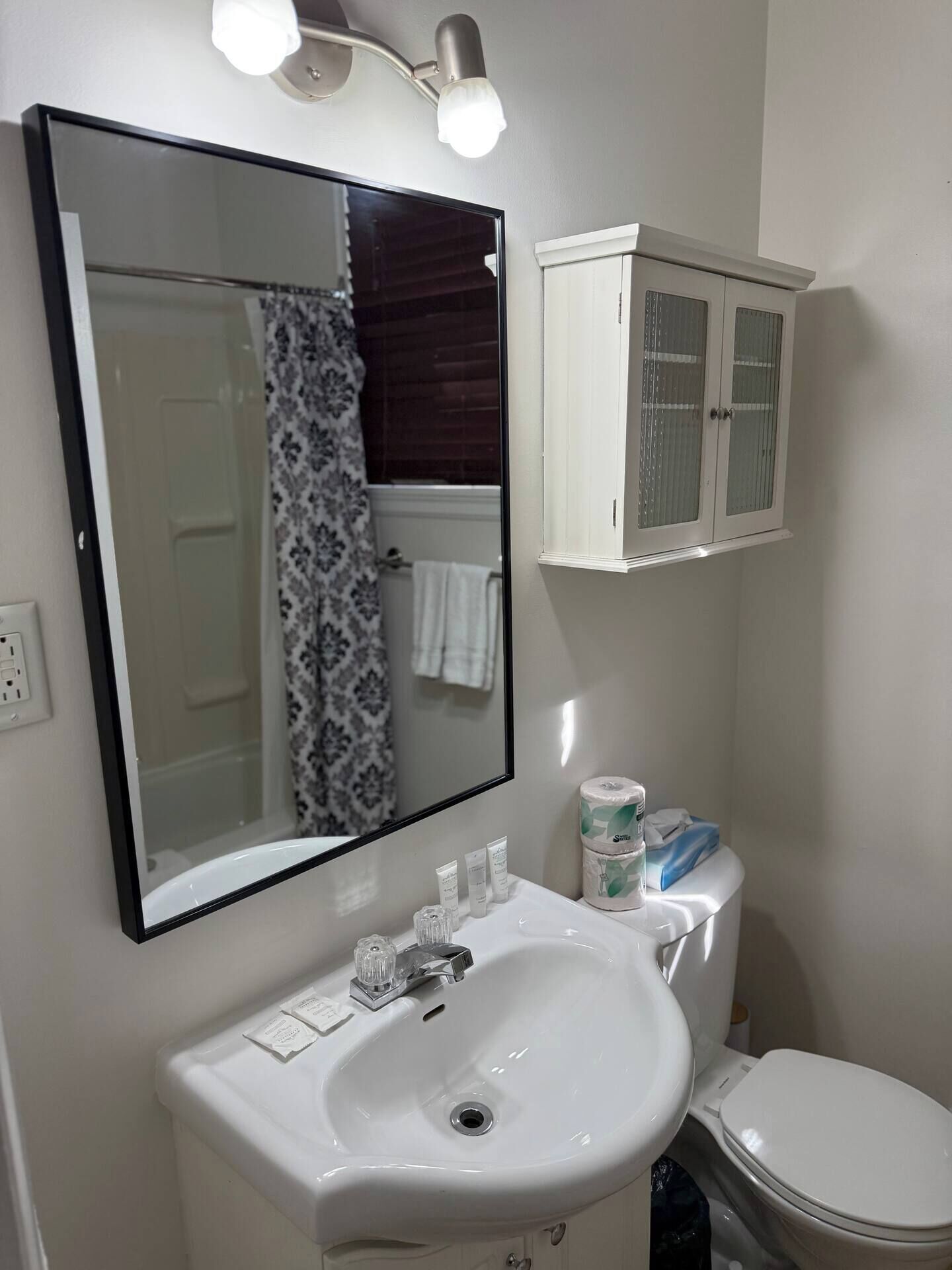 Une salle de bain avec un lavabo blanc, un miroir avec éclairage intégré, des toilettes et un meuble avec des portes en verre.