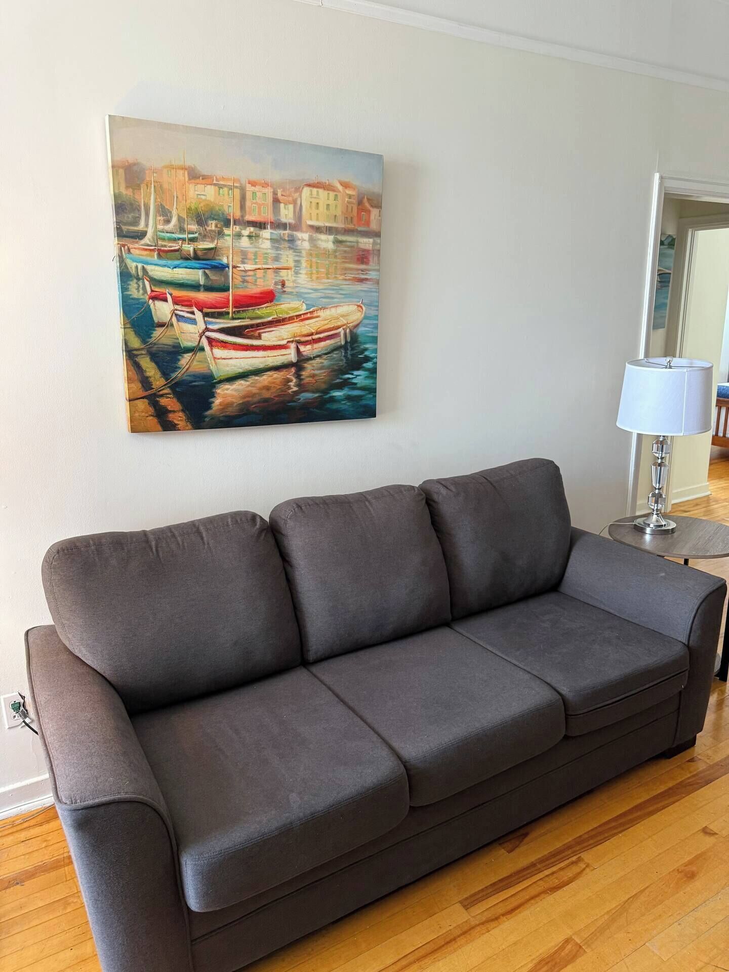 Ein graues Sofa in einem Raum mit einem Bild von Booten an der Wand und einer Lampe auf einem Beistelltisch.