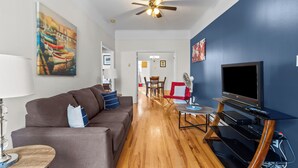A living room with a sofa, TV, and wooden flooring. - Charming 2BR Wi-Fi Off-Street Parking (St. John's)