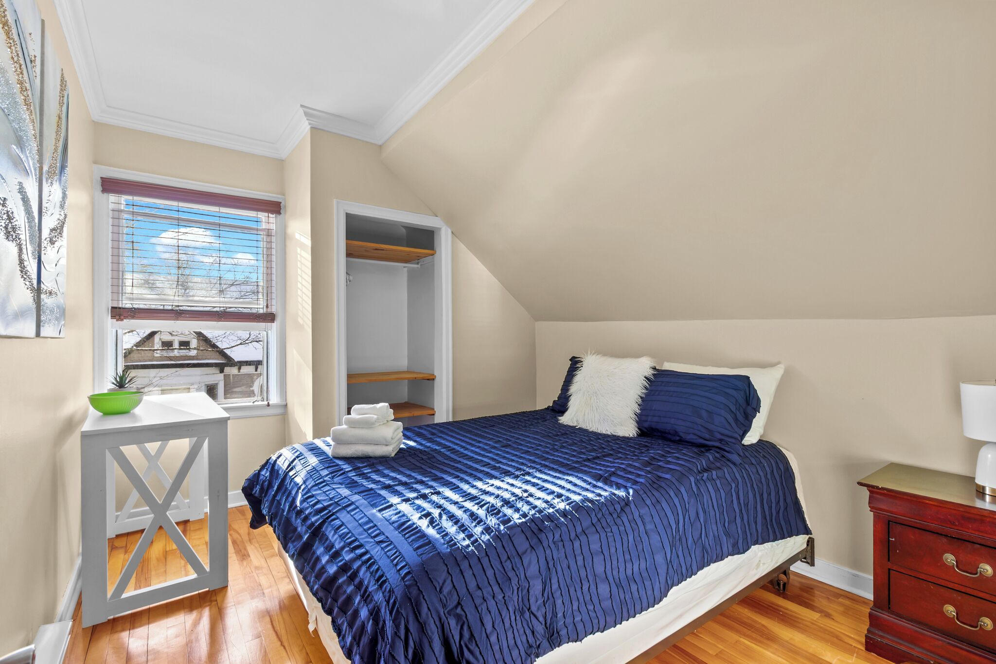 A bedroom with a bed, a window, a small table, and a dresser.