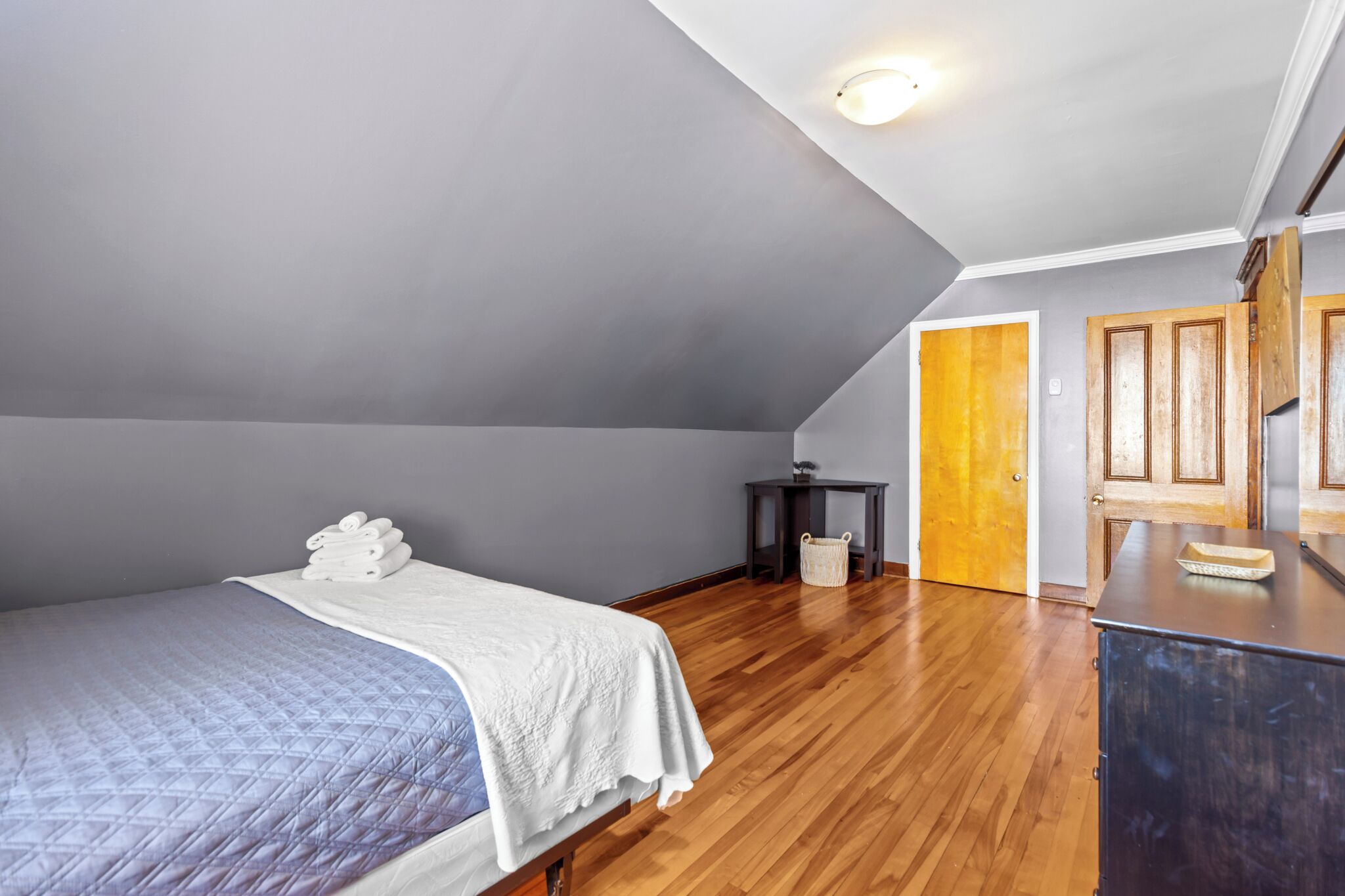 A bedroom with a bed, a nightstand, a wooden dresser, and a door leading to another room.