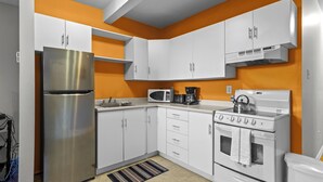 Une cuisine compacte avec des meubles blancs, un réfrigérateur en acier inoxydable, un four à micro-ondes, une machine à café et une cuisinière.