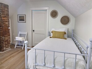 A bedroom with a white bed, a white metal headboard, a white door, and a brick wall. - Yellow House - Downtown & 7 Mins to Cedar Point (Sandusky)