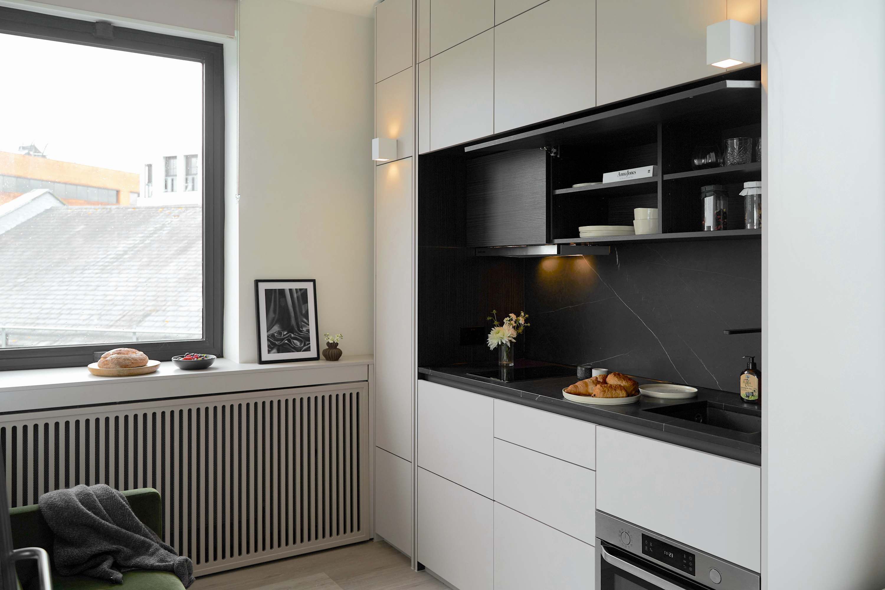 Eine moderne Küche mit Fenster, Heizkörper, einem gerahmten Bild und einer Arbeitsfläche mit Lebensmitteln.