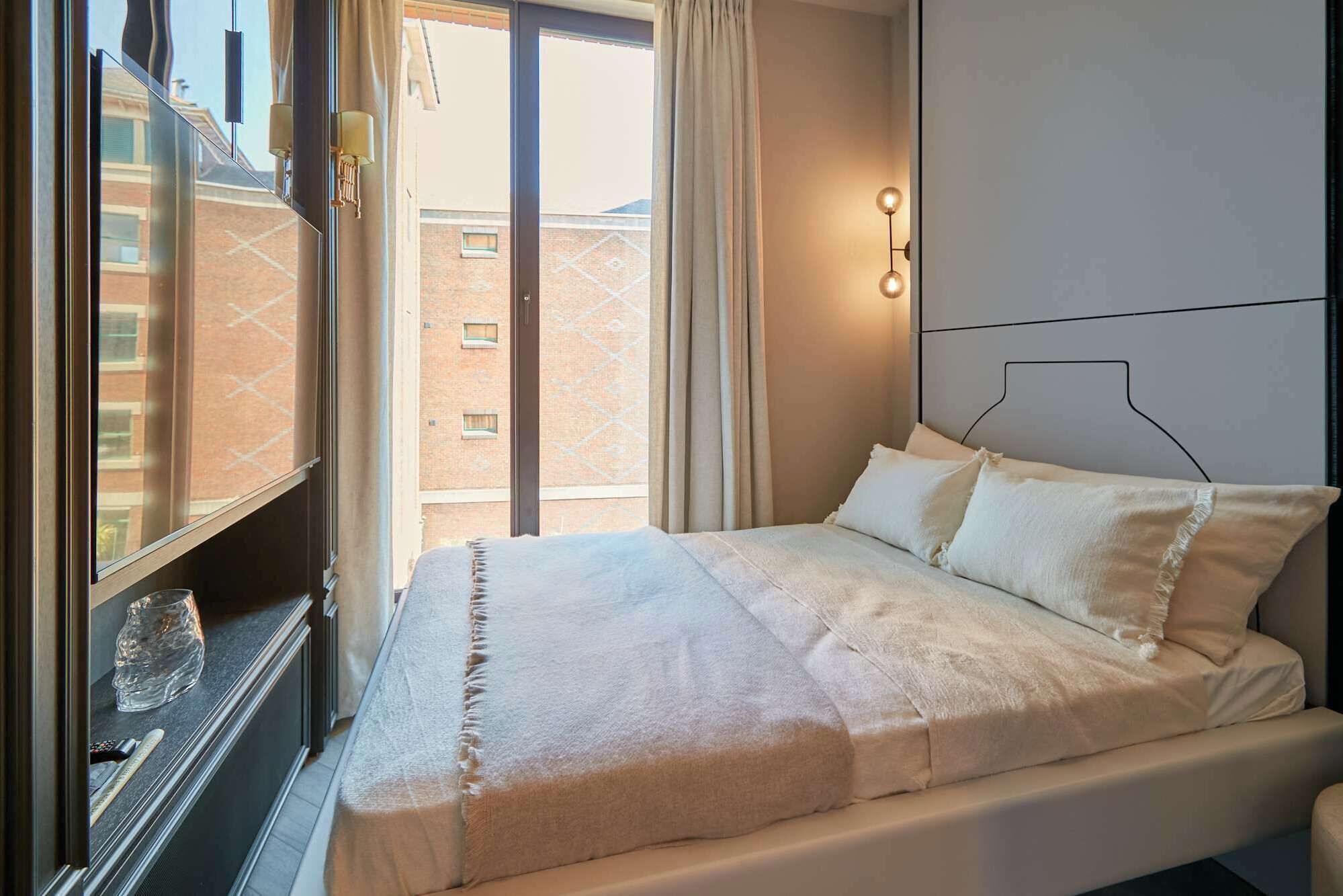Quarto com cama, janela e vista para edifícios.