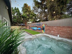 A hot tub area with a mural on the wall, surrounded by greenery and string lights. - CA4. Hot Tub, Mini Golf, Arcade  & EV Charger (Long Beach)