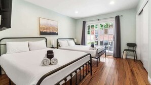 Een hotelkamer met twee bedden, een tafeltje, een stoel, een foto aan de muur en een raam met uitzicht.