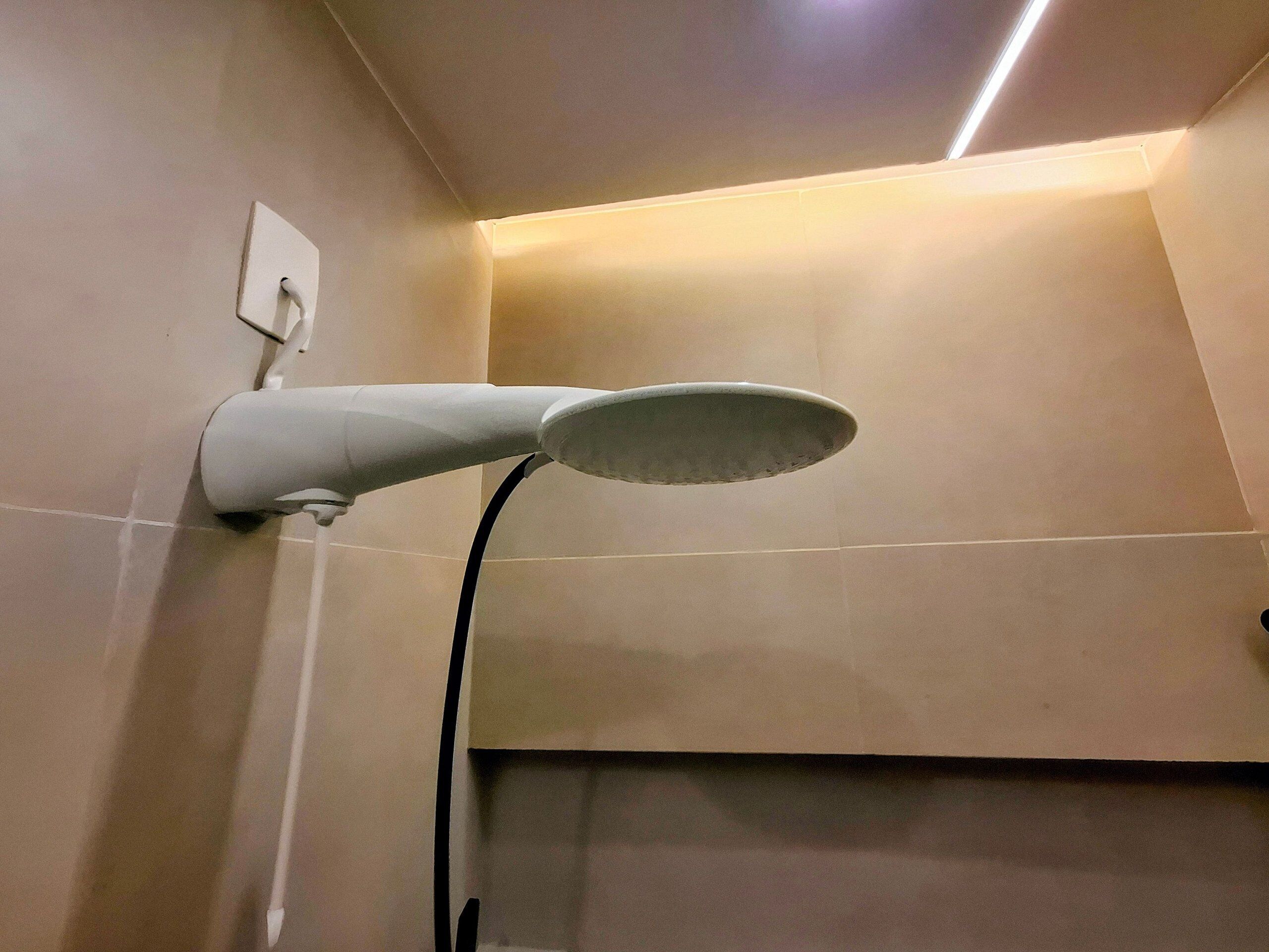 A modern bathroom with a wall-mounted showerhead and a visible electrical outlet.