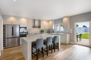 Une cuisine moderne dotée d’un îlot central, d’appareils électroménagers en acier inoxydable et offrant une vue sur l’extérieur.