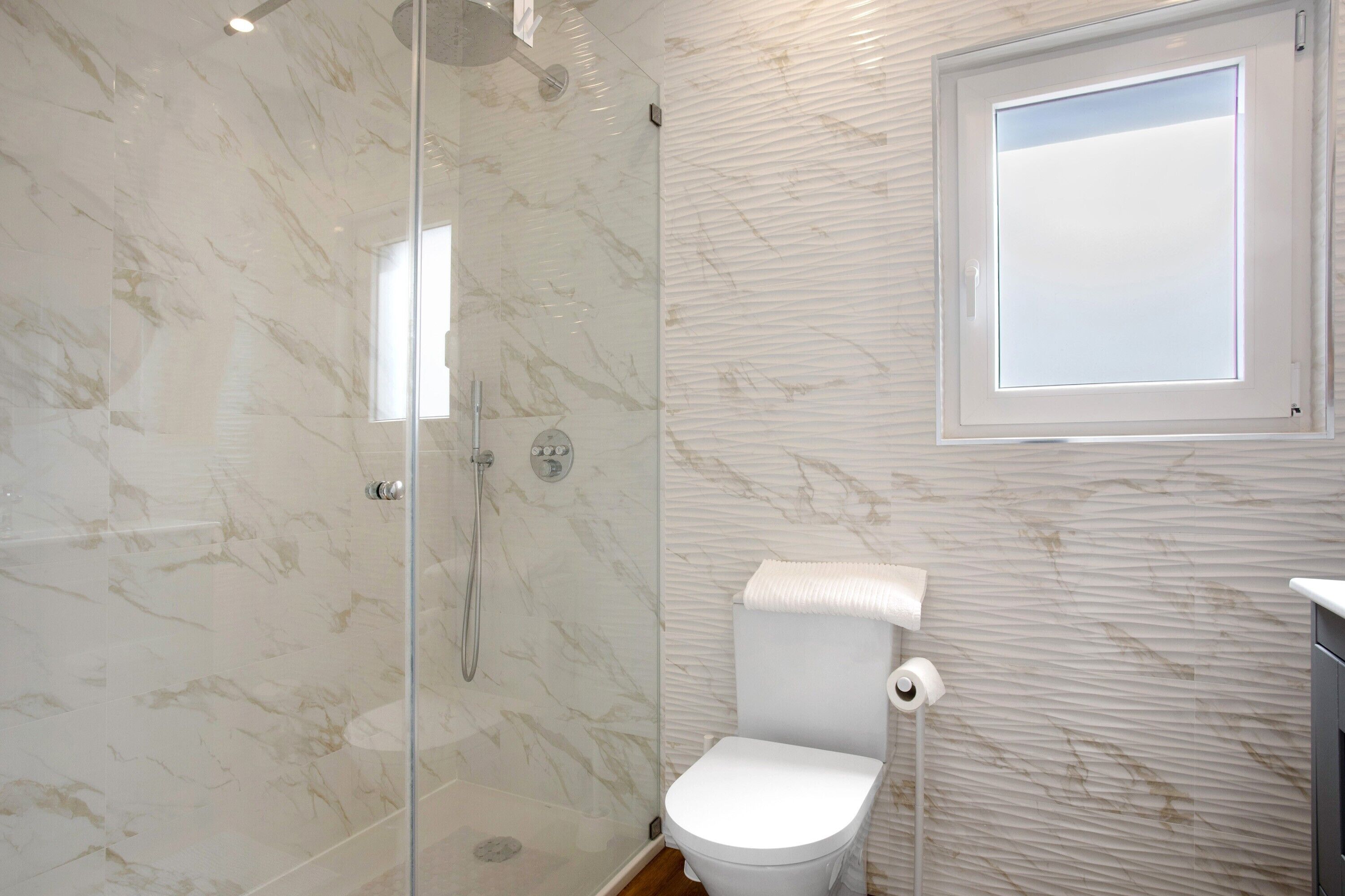 A bathroom with a glass shower enclosure, a toilet, and a window.