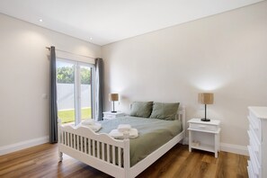 Une chambre à coucher comprenant un lit, des tables de chevet, une commode et une porte-fenêtre coulissante donnant sur un balcon.