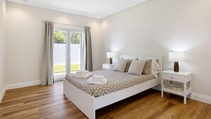 Quarto com cama, mesas de cabeceira, luminária e vista através de uma porta de vidro.