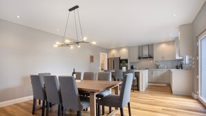 Cozinha moderna com armários brancos, uma ilha central e uma área de jantar com mesa de madeira e cadeiras cinzas.