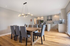 A modern kitchen with white cabinets, a central island, and a dining area with a wooden table and grey chairs.