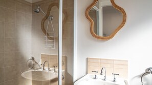 Ein Badezimmer mit Duschkabine aus Glas, Waschtisch mit Spiegel und Waschbecken.