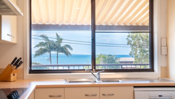 A kitchen with a large window overlooking a beach and palm trees. - Perfectly positioned between Woolgoolga’s beautiful beaches (Woolgoolga)