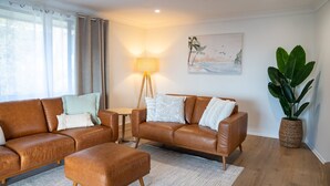 A living room with a brown leather sofa, a small side table, a floor lamp, and a large potted plant. - Perfectly positioned between Woolgoolga’s beautiful beaches (Woolgoolga)