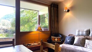 Une pièce chaleureuse avec une table en bois, un canapé agrémenté de coussins à motifs, une fenêtre avec des rideaux et une lampe fixée au mur.