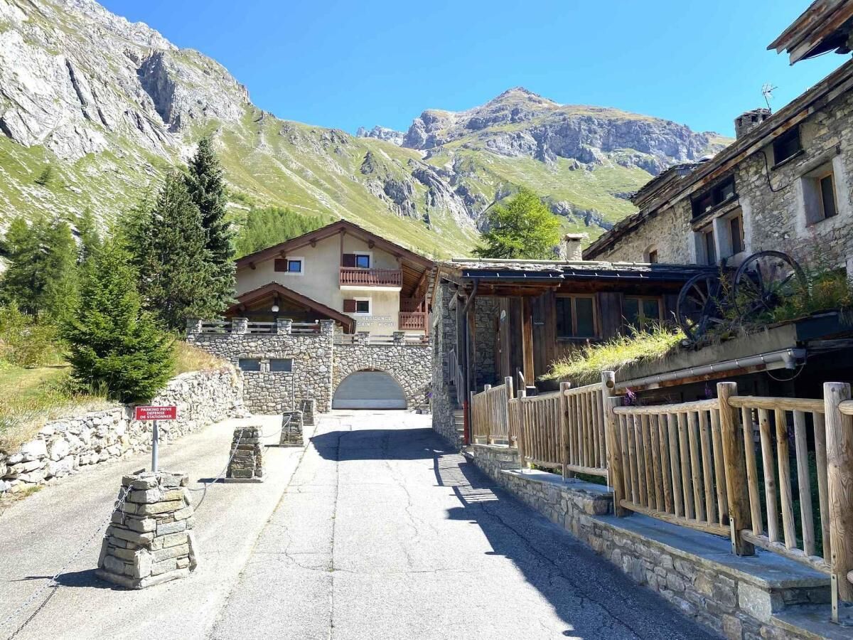 A mountain road leading to a stone building with a wooden fence and a sign indicating a restaurant.