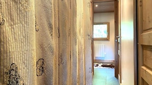 Un couloir intérieur en bois, au décor rustique, avec une porte dotée d’une poignée et une fenêtre laissant entrer la lumière naturelle.