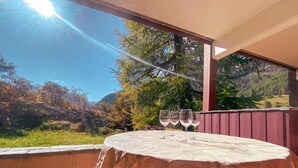 Une table recouverte d’une nappe à motifs, avec trois verres à vin, sur un balcon offrant une vue sur la montagne.