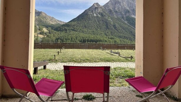 Ein Balkon mit zwei roten Stühlen, der auf eine gebirgige Landschaft blickt.