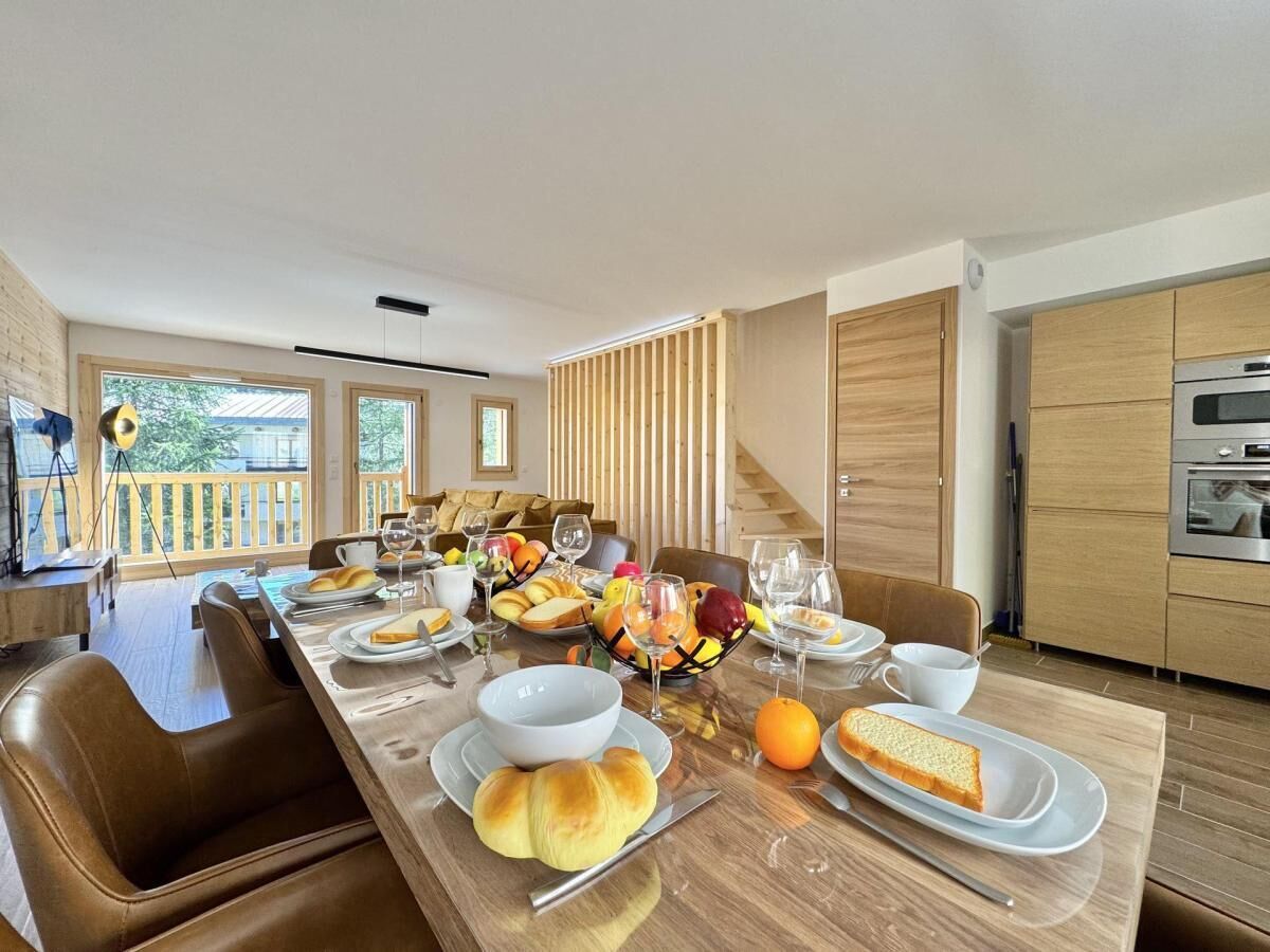 Un espace repas moderne avec une longue table en bois dressée pour un repas, entourée de chaises en bois.