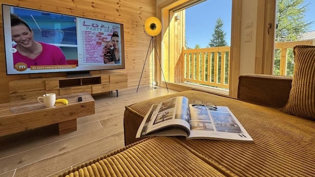 Una camera moderna con una parete in legno, un'ampia finestra, una televisione, una rivista e un tavolino con una tazza e una banana.