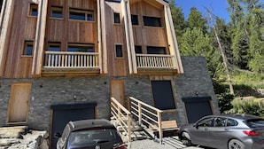 Un edificio in legno a più piani con balconi, pareti in pietra e un'auto parcheggiata di fronte.