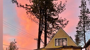 Una casa con terraza de madera, un perro en el jardín y un cielo al atardecer.