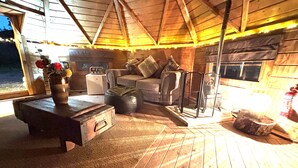 A cozy interior with a wooden ceiling, a sofa set, a table with a vase, and a fireplace. - Hobbit Haven Hot Tub and Countryside Bliss (Gaerwen)