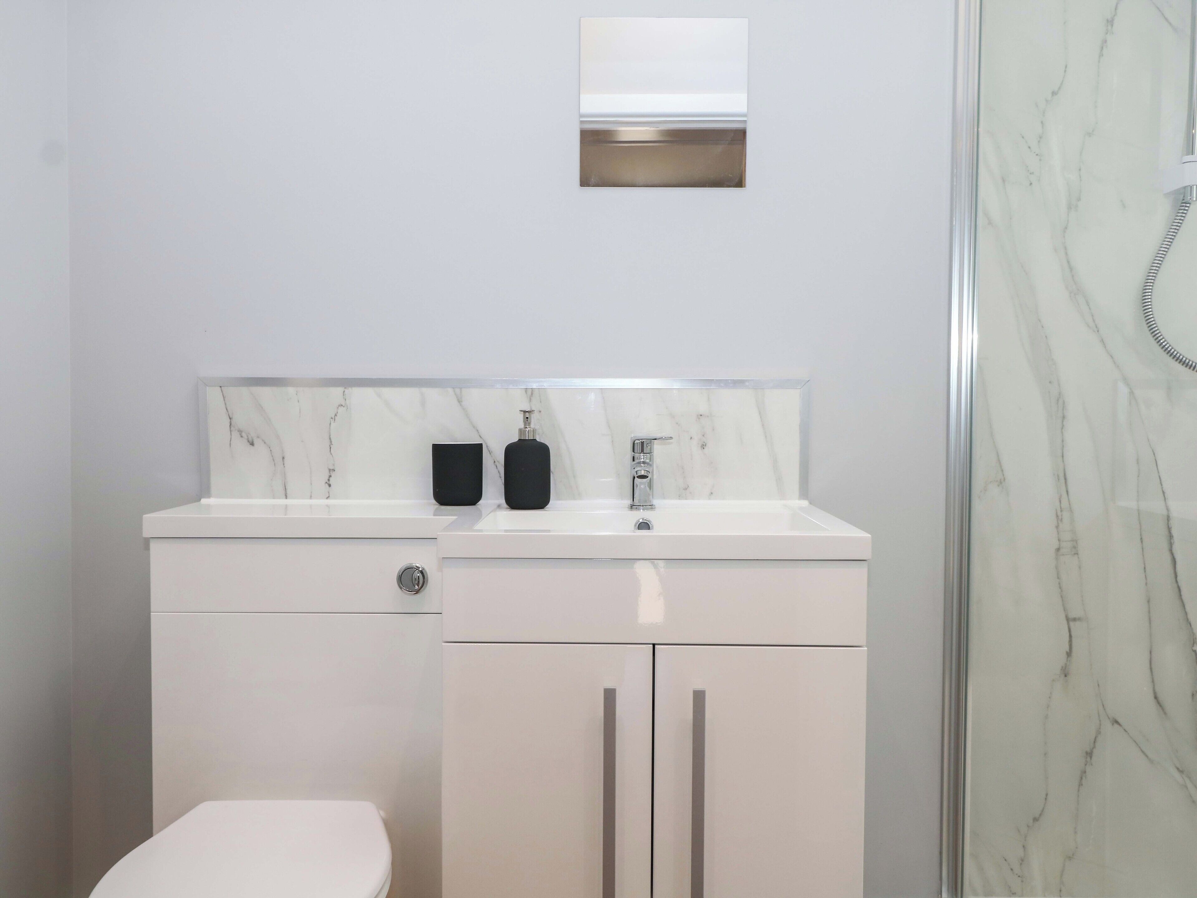 A modern bathroom with a white marble sink, a toilet, and a shower.