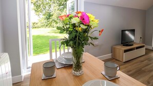 A modern living room with a dining table, a vase of flowers, a television, and a view of a garden through a glass door. - The Old Parlour (Southampton)