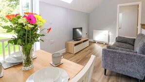 A modern living room with a wooden dining table, a grey sofa, a TV, and a white radiator. - The Old Parlour (Southampton)