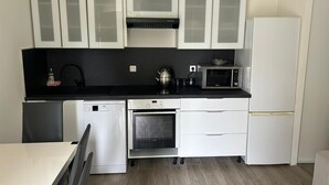 A modern kitchen with white cabinets, a black countertop, a microwave, a kettle, and a dishwasher. - Studio 4 persons (Le Cannet)