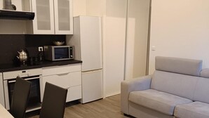 A compact kitchen with white cabinets, a microwave, a kettle, and a refrigerator. There is a dining table with chairs and a sofa in the living area. - Studio 4 persons (Le Cannet)
