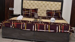 Un letto con testiera trapuntata, due cuscini coordinati, una coperta a letto fantasia scura e un comodino con una lampada.