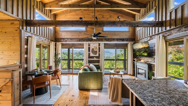 A spacious wooden cabin with a dining area, a cozy seating area, and a kitchen with large windows offering scenic views. - Secluded Couples' Cabin - Fire pit, Hot Tub, Location, Views (Gatlinburg)