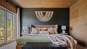 A bedroom with a large bed, a bench, a wall-mounted macrame piece, and a view through a window. - Secluded Couples' Cabin - Fire pit, Hot Tub, Location, Views (Gatlinburg)