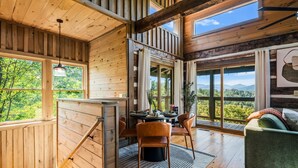 A wooden cabin interior with a dining area, a sofa, and large windows offering a view of the outdoors.