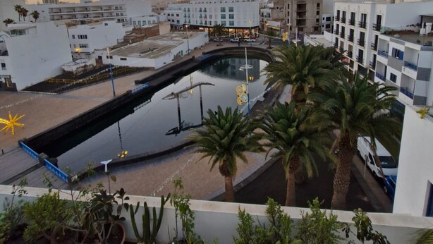 A rooftop with a swimming pool, palm trees, and a view of the cityscape during sunset. - Casa Sofia - Apartment 1 with Mountain Views, Balcony and Wi-Fi (Arrecife)