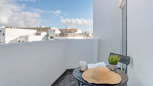 A balcony with a white wall, a small table with a hat, a cup, and a book, and a potted plant. - Casa Sofia - Apartment 1 with Mountain Views, Balcony and Wi-Fi (Arrecife)