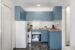 Eine kleine Küche mit blauen Schränken, einer Waschmaschine, einem Backofen und einem Spülbecken.