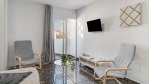 A modern hotel room with a large window, two armchairs, a round coffee table, a flat-screen TV mounted on the wall, and a decorative wall piece. - Casa Sofia - Apartment 1 with Mountain Views, Balcony and Wi-Fi (Arrecife)