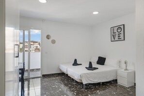 Quarto com cama, mesa de cabeceira, quadro na parede e vista através de uma porta de vidro.