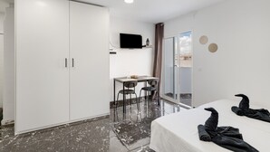 A hotel room with a bed, a desk with chairs, a TV, and a sliding door to a balcony.