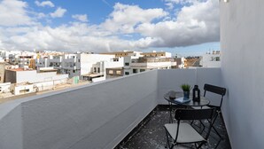A rooftop terrace with a table and chairs, a potted plant, and a view of the cityscape.